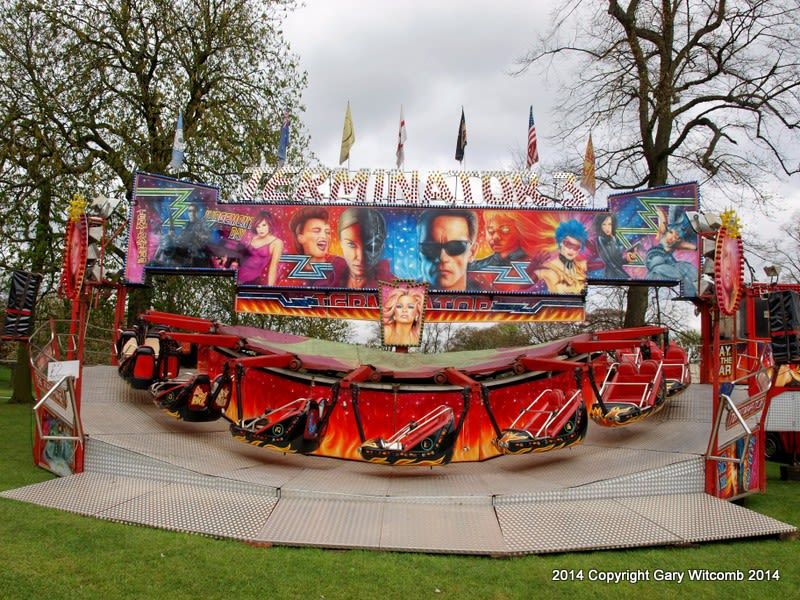 Full Matterhorn ride set up on grass, with red suspended two-seat carts, silver loading deck and a broad painted frontage