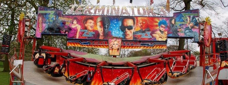 Full Matterhorn ride set up on grass, with red suspended two-seat carts, silver loading deck and a broad painted frontage