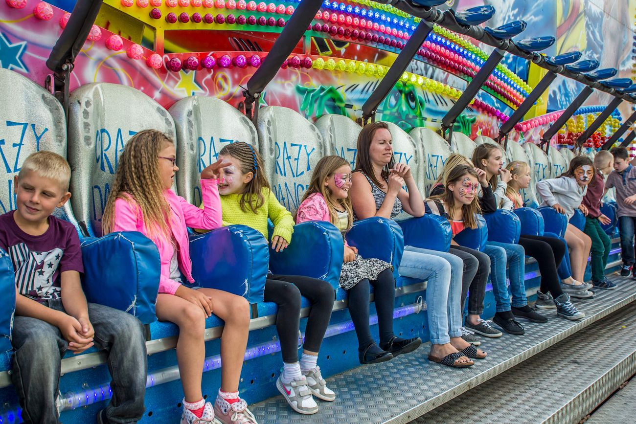 Twenty-place Miami ride bench loaded with adults and children beneath rows of coloured bulbs