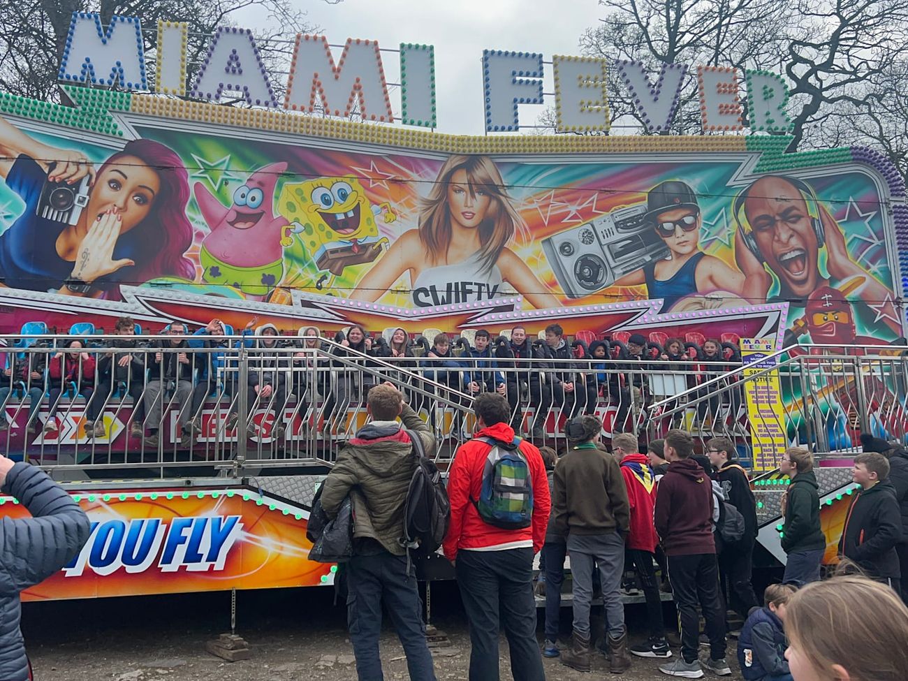 Miami Fever ride loaded at a busy public fair with a queue gathered across the front