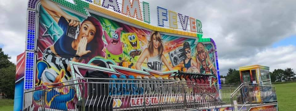 Full Miami Fever ride set up on grass beneath a cloudy sky, with its painted frontage, loading platform and control booth