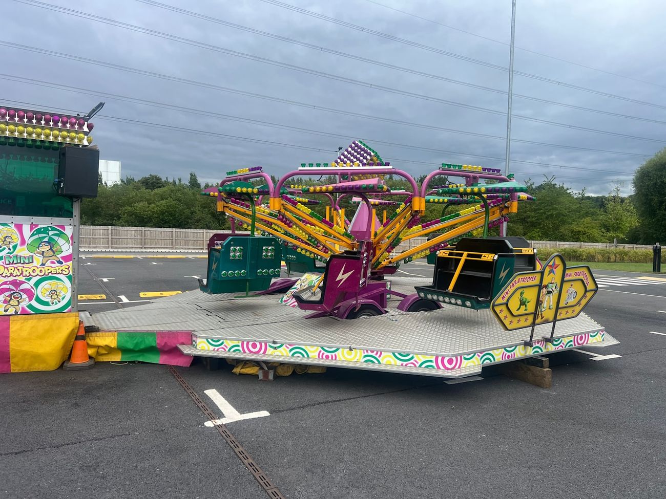 The mini paratrooper ride set up on a paved lot, showing the full structure with magenta and yellow arms