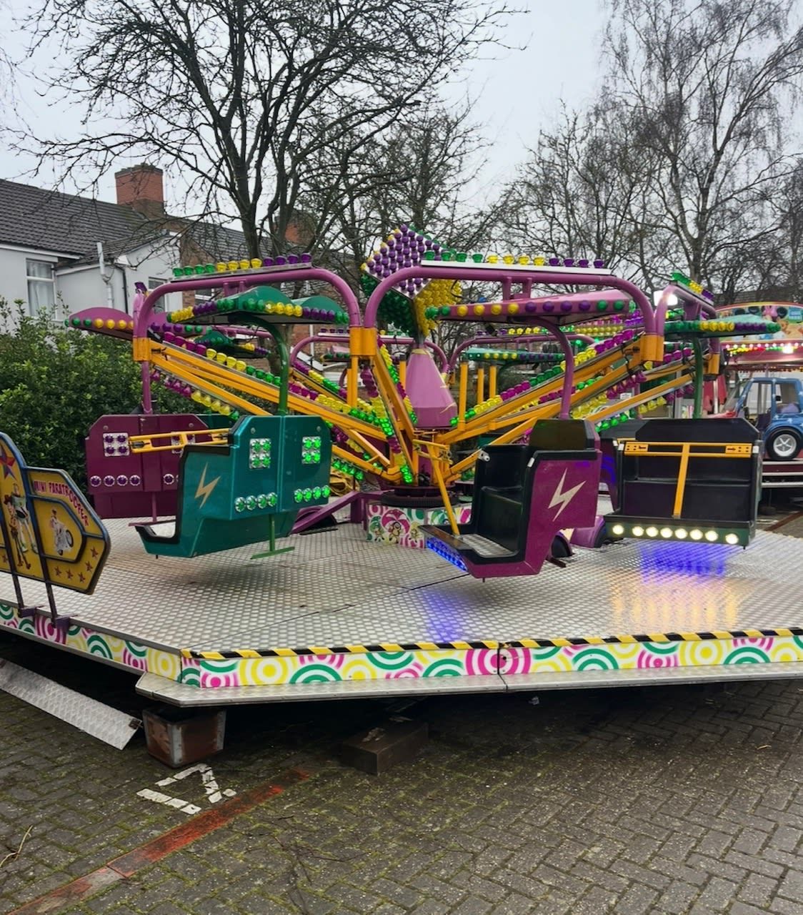 Mini paratrooper children's ride with colourful cabin cars on bulb-lit arms, set up on a raised platform