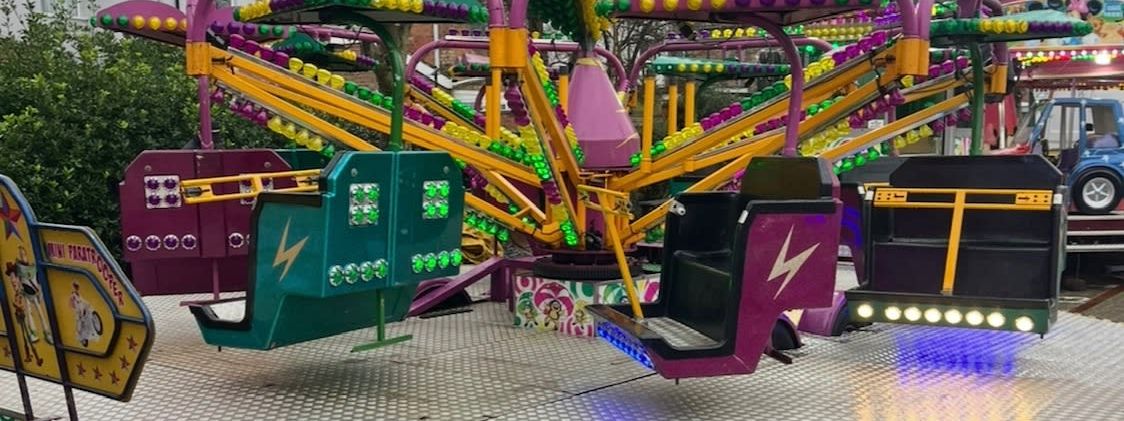 Mini paratrooper children's ride with colourful cabin cars on bulb-lit arms, set up on a raised platform