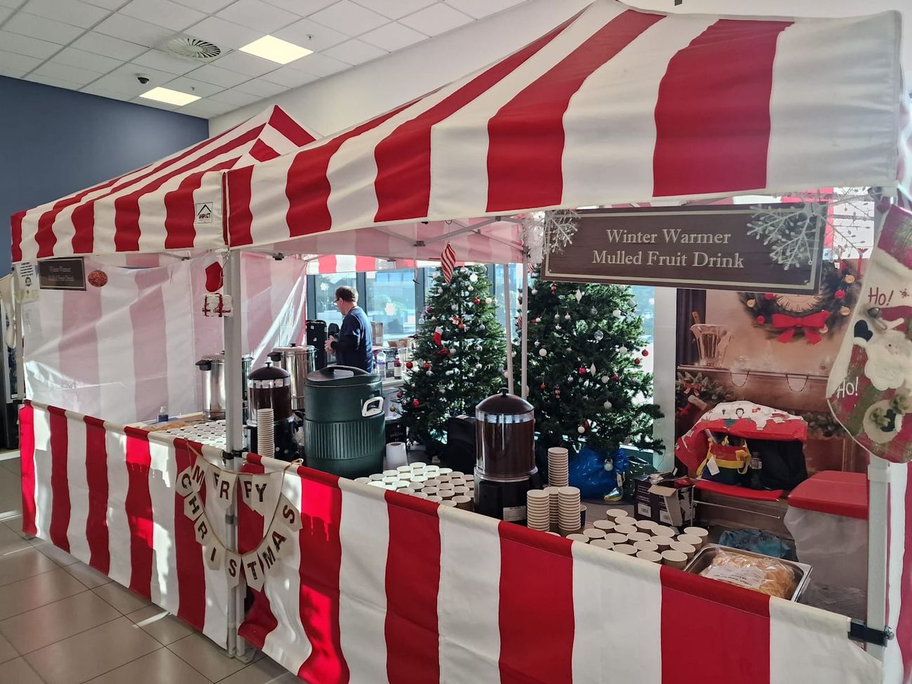 Mulled wine stall set up indoors for a festive event, with striped canopy and serving table