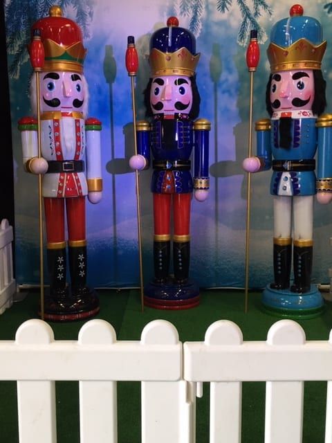 Three nutcracker trail figures behind a white picket fence with a winter backdrop