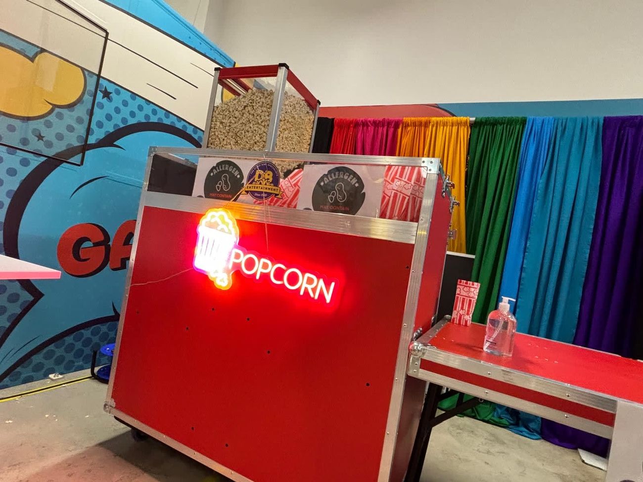 Red flight-case popcorn cart with its glowing neon POPCORN sign and the machine behind the glass