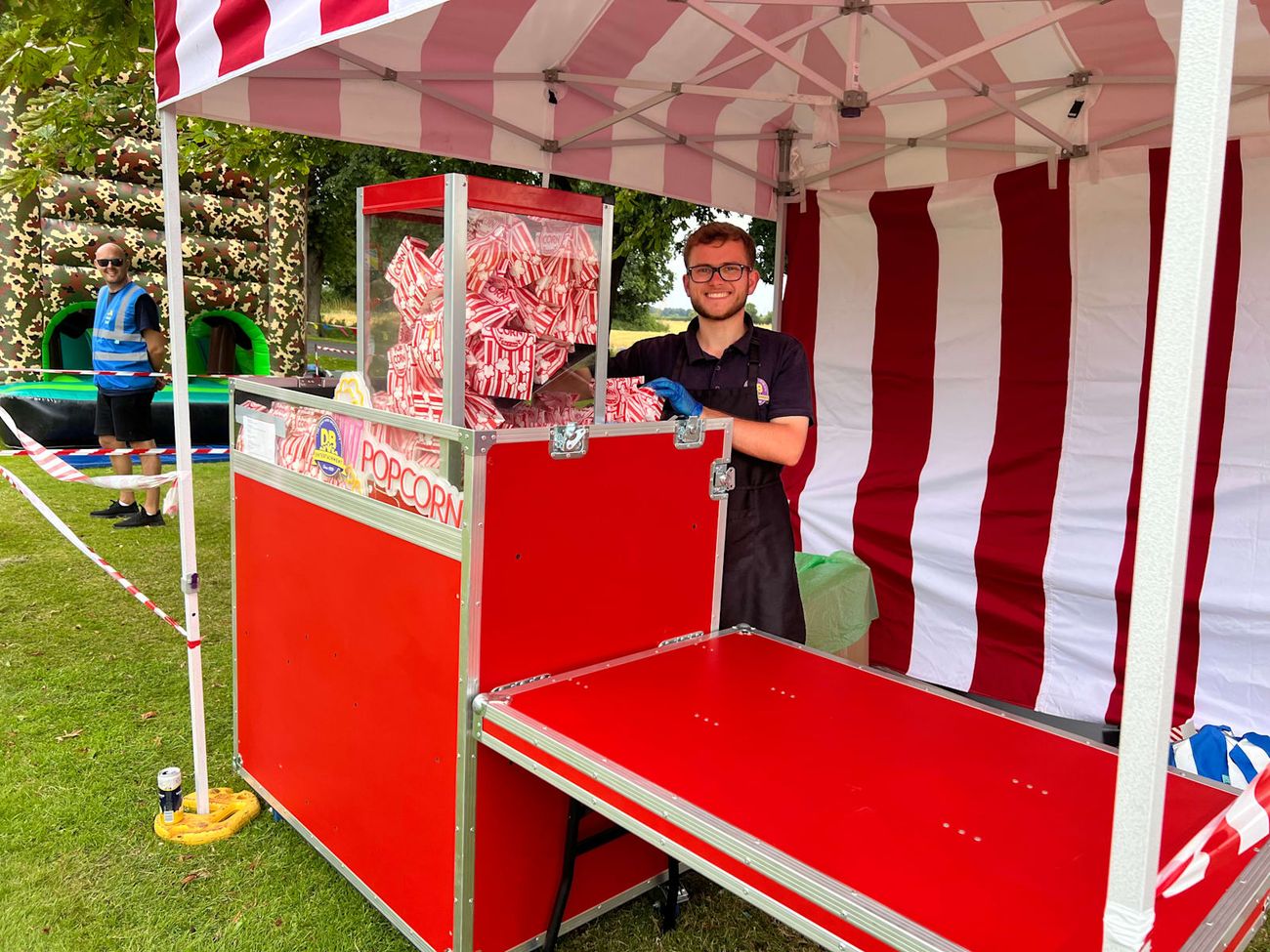Red popcorn cart with a vendor serving freshly popped popcorn in striped bags at an outdoor event