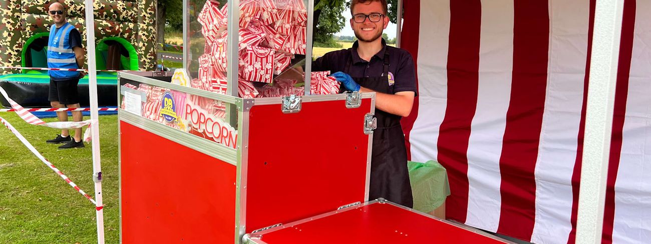 Red popcorn cart with a vendor serving freshly popped popcorn in striped bags at an outdoor event