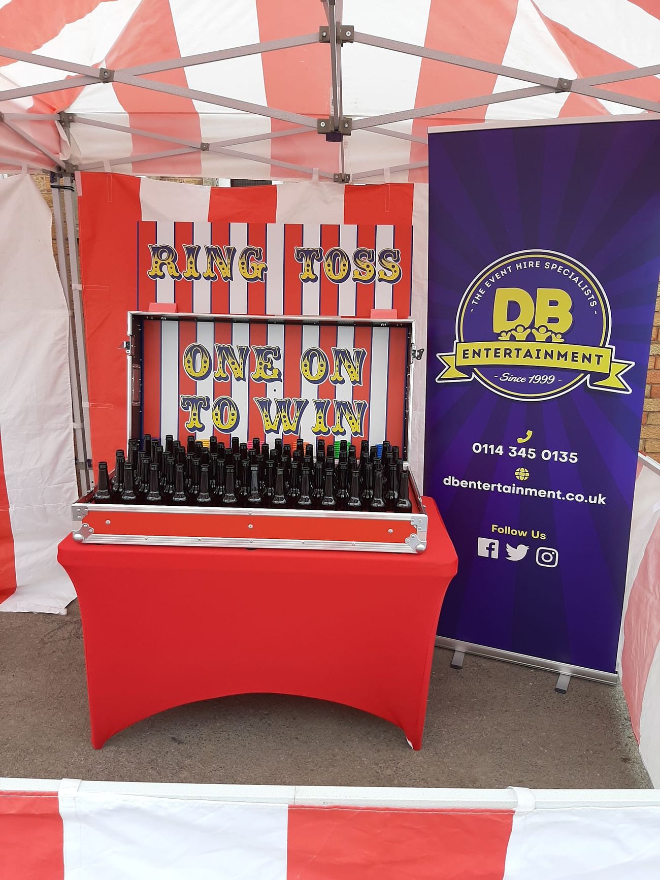 Ring Toss stall under its red and white striped canopy, with bottles packed into the flight case and rings ready to throw