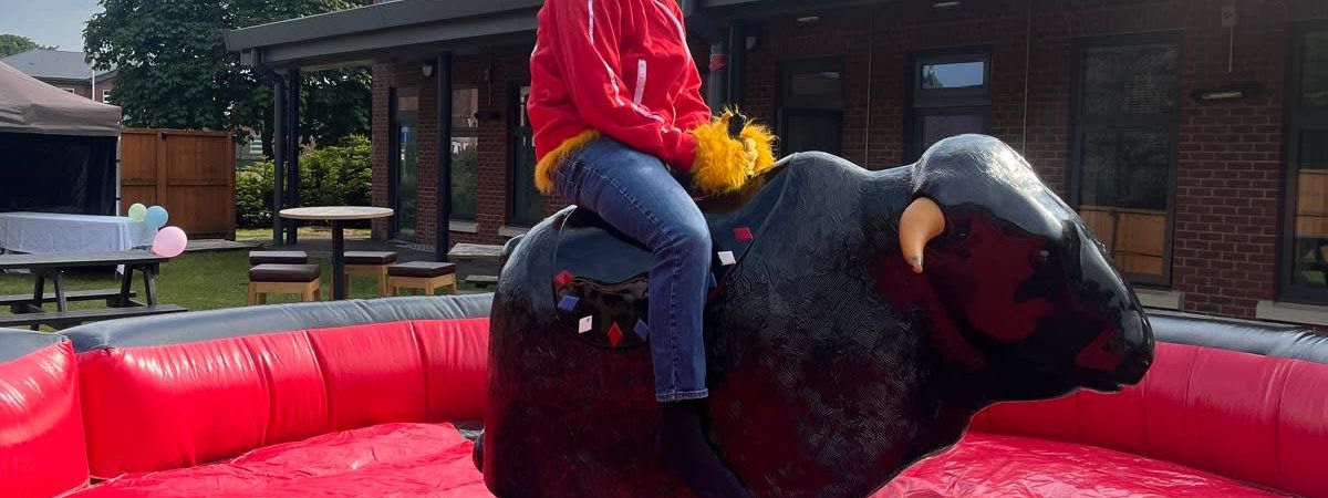 A rider in a mascot head holding on to the rodeo bull at a corporate event