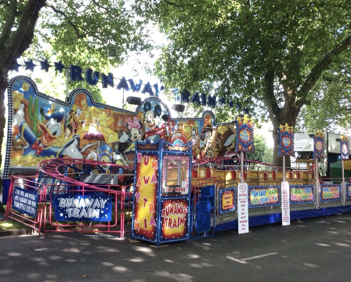 Runaway Train funfair ride on tarmac beneath trees, with its painted wild-west frontboard and star-decked lettering