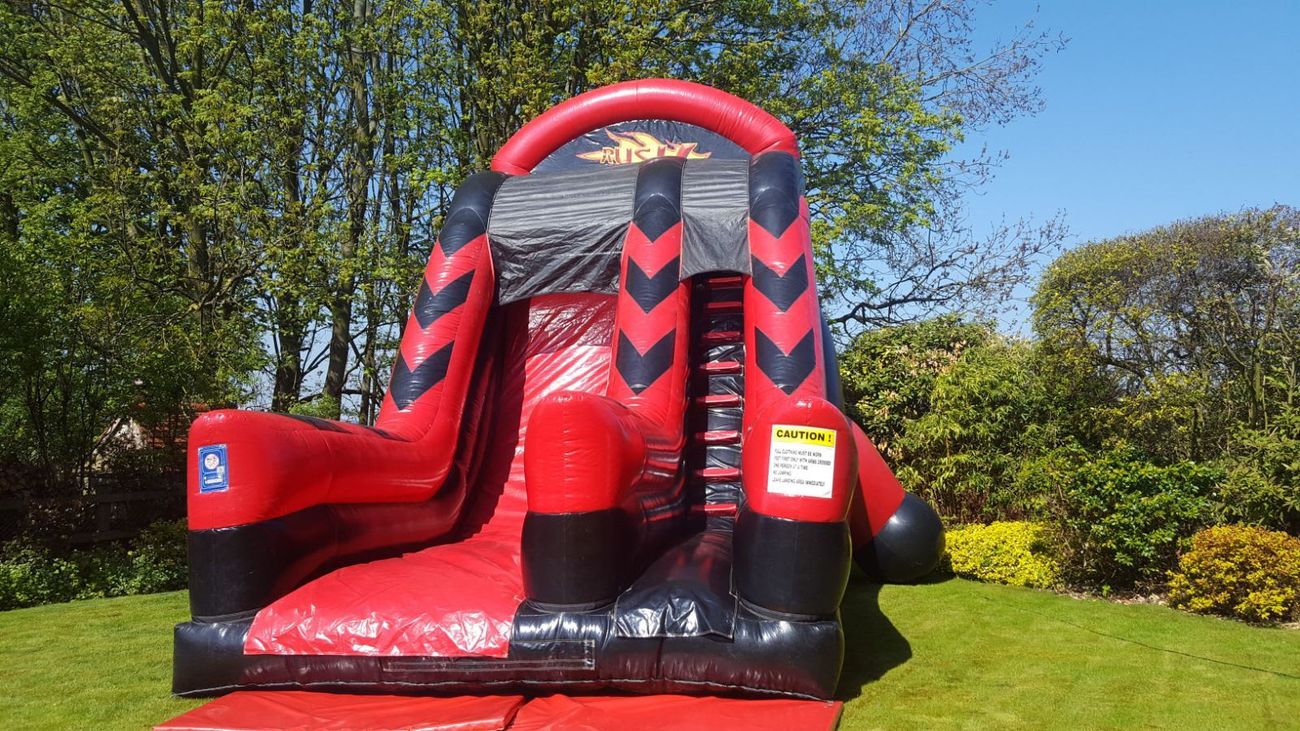 Rush Mega Slide inflatable set up outdoors, showing the red and black structure with its climb, arch and steep slide