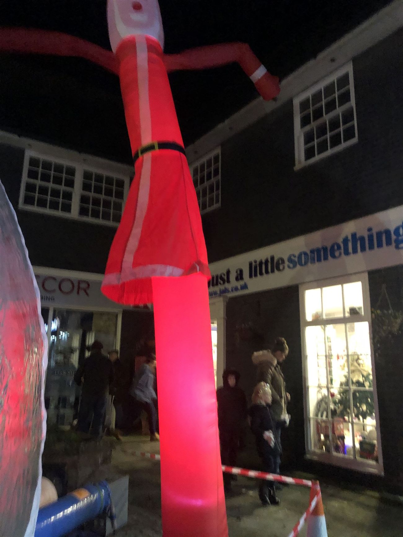 The Santa sky dancer glowing bright red at night, with Christmas shop window displays below