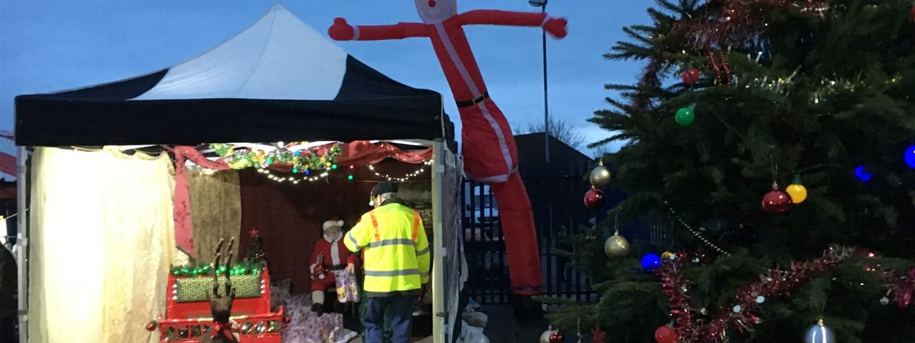 The Santa sky dancer towering over a Christmas grotto marquee at dusk, with a decorated tree and string lighting