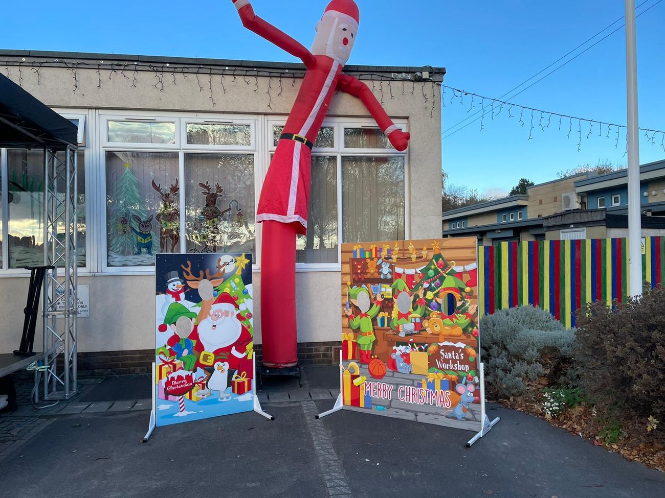 The Santa sky dancer waving beside Christmas selfie boards at a school event, with festive window decorations overhead