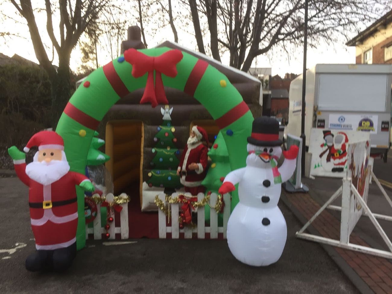 Front of the inflatable Santa's grotto with a waving Santa, snowman prop and wreath arch over the entrance