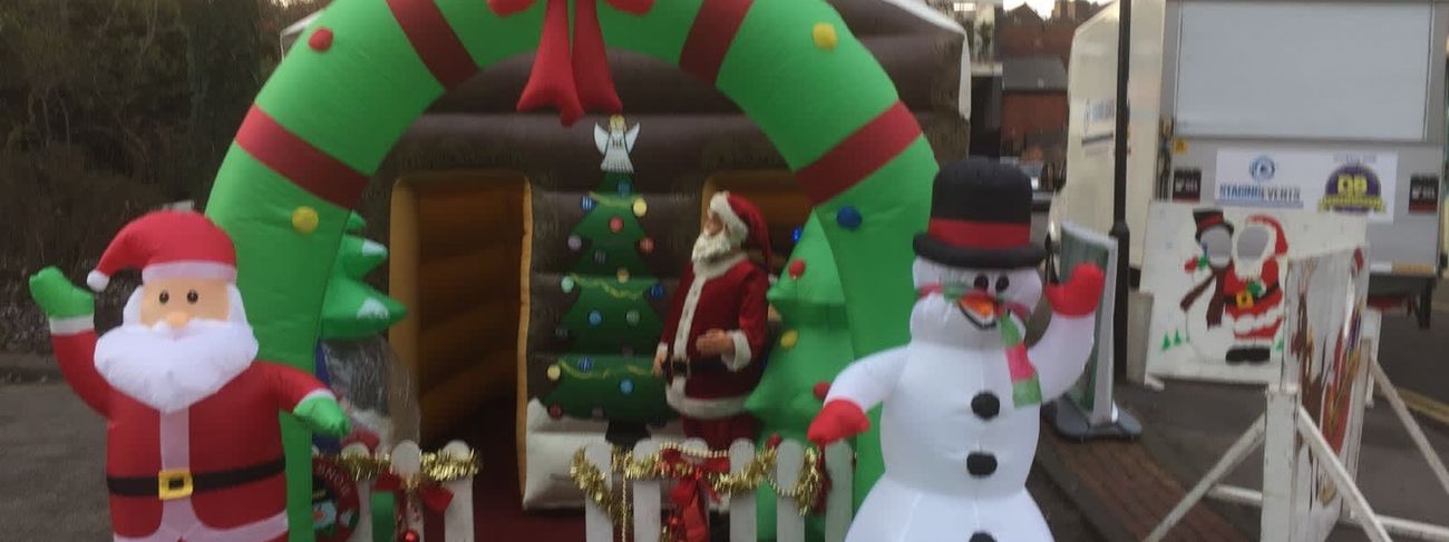 Front of the inflatable Santa's grotto with a waving Santa, snowman prop and wreath arch over the entrance