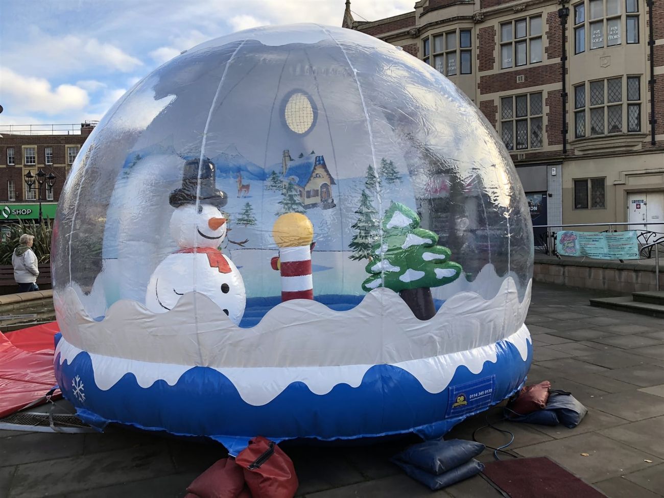 Inflatable snow globe photo pod set up in a town square, with the snowman and tree visible through the clear dome