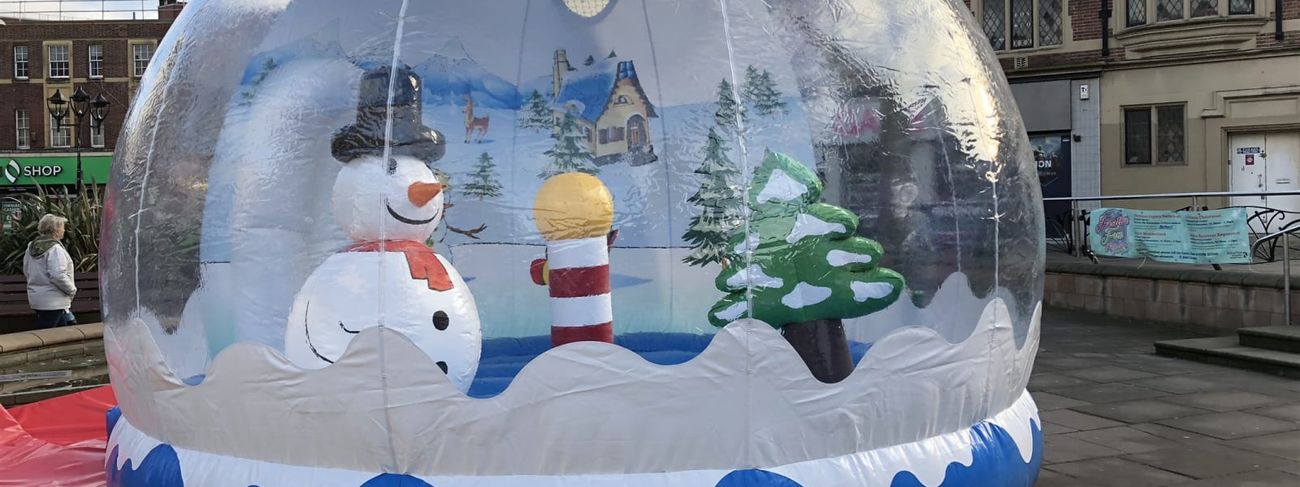 Inflatable snow globe photo pod set up in a town square, with the snowman and tree visible through the clear dome