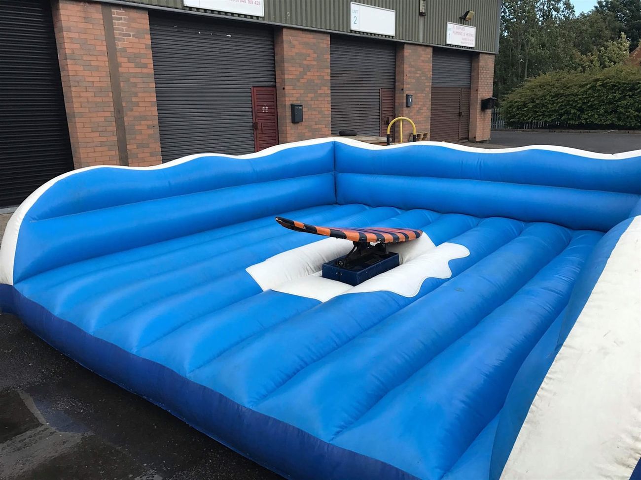 Full surf simulator inflatable structure showing the surfboard platform in the centre of the blue wave-edged bed