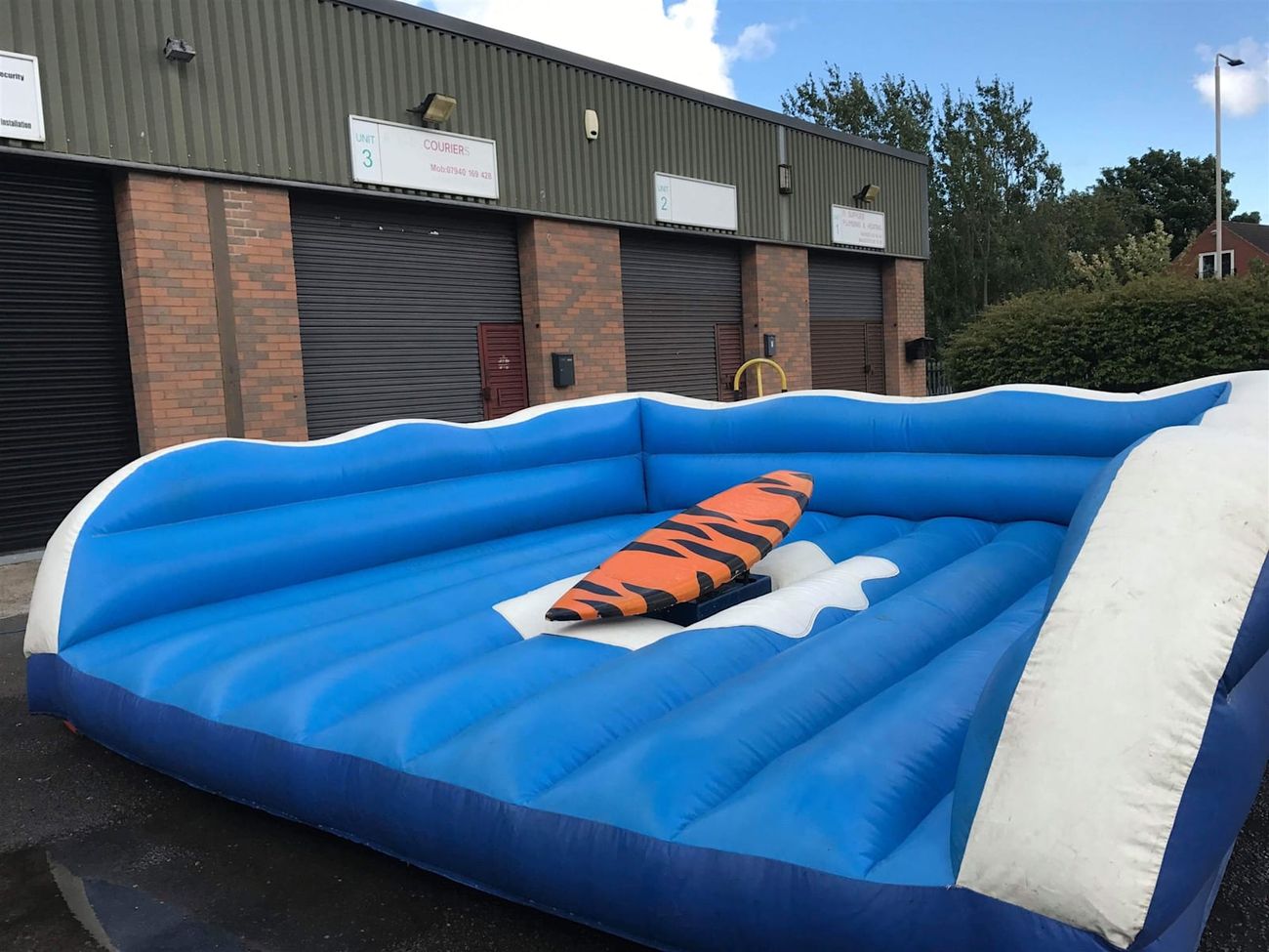 Surf simulator ride on its inflatable bed outdoors, showing the surfboard platform and blue wave-edged surround