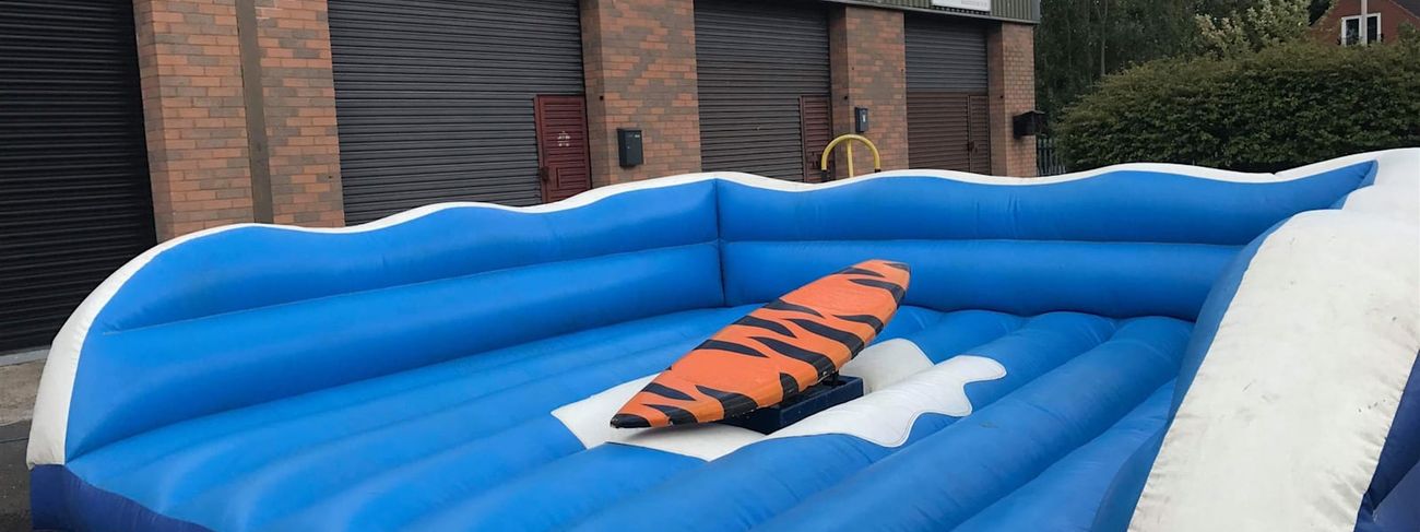 Surf simulator ride on its inflatable bed outdoors, showing the surfboard platform and blue wave-edged surround