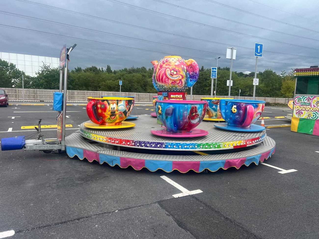The central teapot painted with the Cheshire Cat, with red, blue and yellow teacups circling it on their saucers