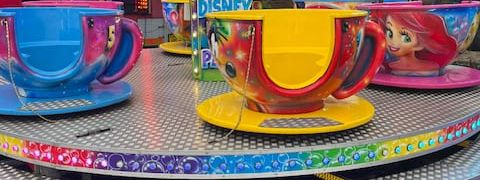 Tea cup ride with character-painted cups on saucers around a central teapot, set up on block paving