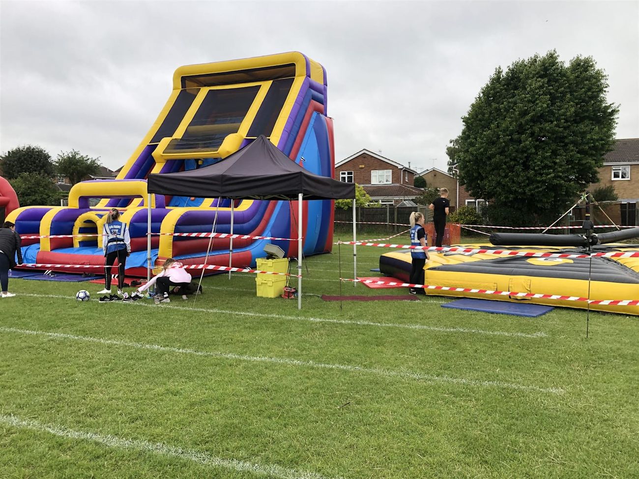 The Tallest Mega Slide standing on an event field, showing the full scale against surrounding houses and trees