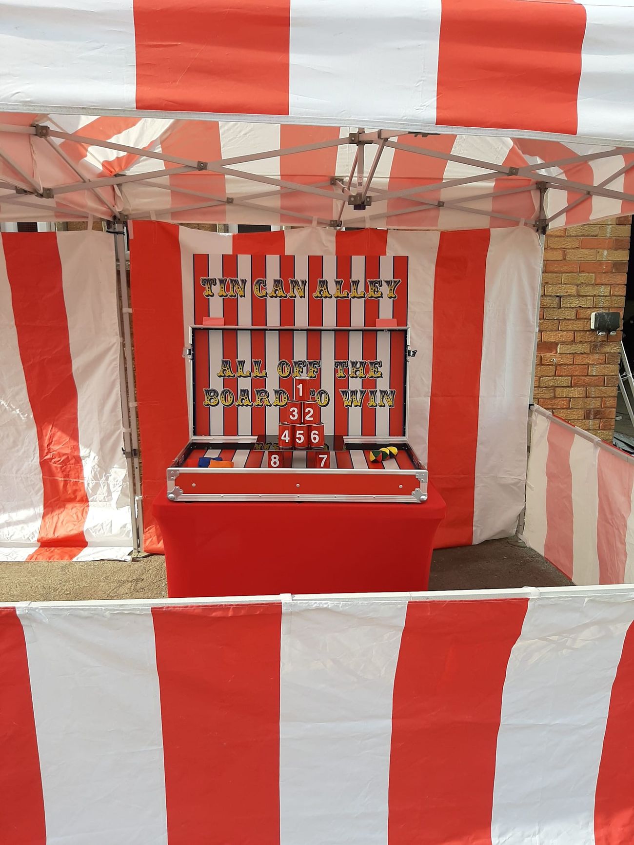 The red and white Tin Can Alley stall front with the game unit on its table, ready for players