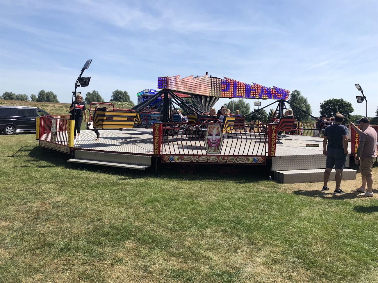 Front of the Twister at an outdoor event with riders aboard, entrance steps, fenced platform and illuminated centre sign