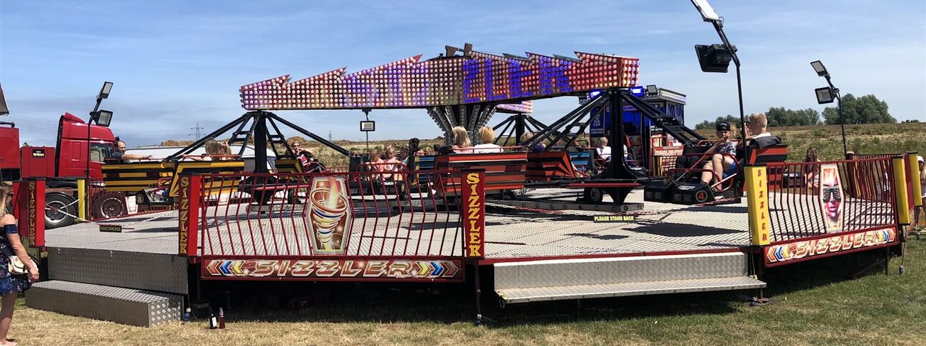 Twister Sizzler ride operating on grass with riders in red and yellow bench cars around the illuminated centre
