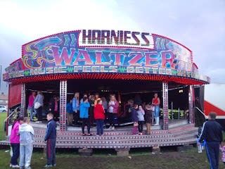 Andrew Harniess's covered Waltzer at an outdoor evening event, with its illuminated frontage and guests on the loading platform
