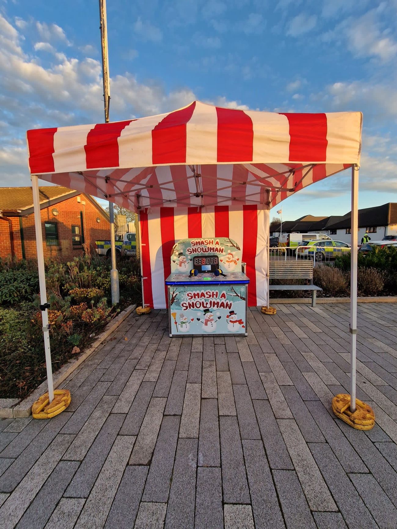 The Whack a Snowman cabinet set up outdoors under a red-and-white striped gazebo on paving stones